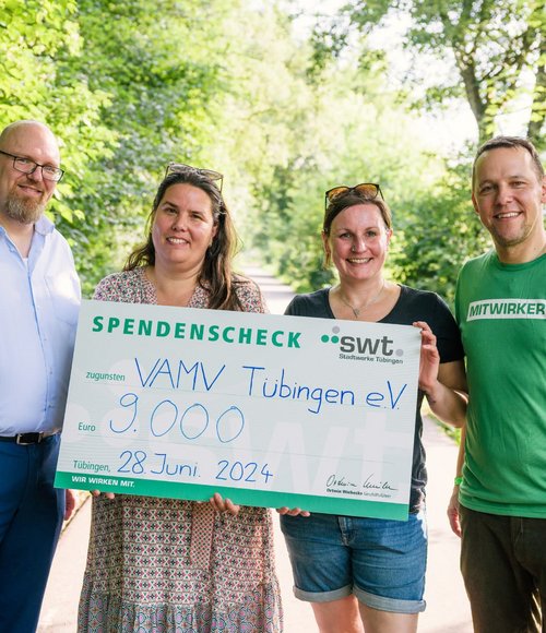 Vier Personen stehen im Grünen und halten einen übergroßen symbolischen Spendenscheck über 9.000 Euro für den Verein VAMV Tübingen e.V. mit dem Logo der Stadtwerke Tübingen. Der Scheck ist auf den 28. Juni 2024 datiert.