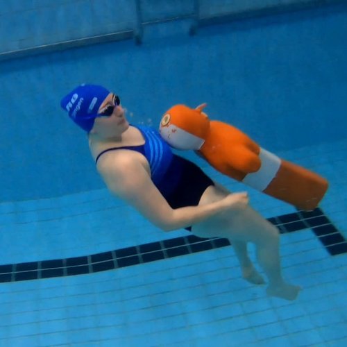 Eine Person trägt eine blaue Badekappe und schwimmt unter Wasser mit einem orangefarbenen Schwimmrettungsgerät