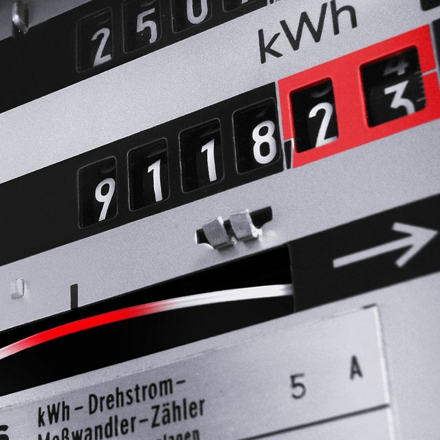 Ein Stromzähler zeigt eine Ablesung von 91182 kWh an. Der Zähler hat schwarze Ziffern auf einem silbernen Hintergrund, und einige Zahlen sind rot hervorgehoben. Es gibt auch ein gewundenes Metallband und eine Pfeilgrafik auf der rechten Seite des Zählers.