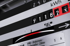 Ein Stromzähler zeigt eine Ablesung von 91182 kWh an. Der Zähler hat schwarze Ziffern auf einem silbernen Hintergrund, und einige Zahlen sind rot hervorgehoben. Es gibt auch ein gewundenes Metallband und eine Pfeilgrafik auf der rechten Seite des Zählers.