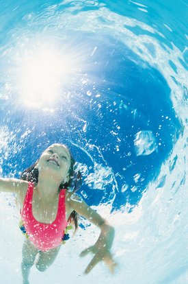 Ein Mädchen mit braunen Haaren trägt einen pinken Badeanzug und schwimmt unter Wasser, umgeben von Blasen und Licht.