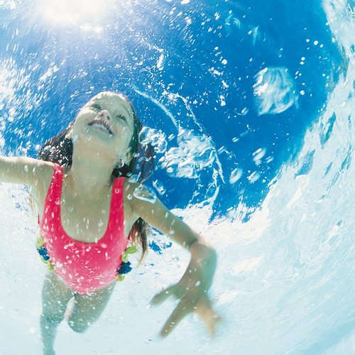 Ein Mädchen mit braunen Haaren trägt einen pinken Badeanzug und schwimmt unter Wasser, umgeben von Blasen und Licht.