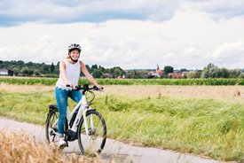 Eine Frau mit einem schwarzen Fahrradhelm sitzt auf einem Mountainbike und lächelt vor einer Blumenwiese